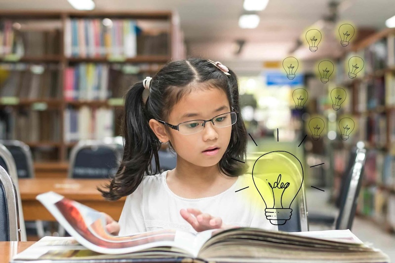 Young girl reading a book in a library - Literacy skills reading