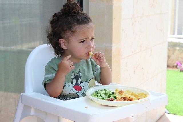 small toddler girls sitting in a high chair eating by herself